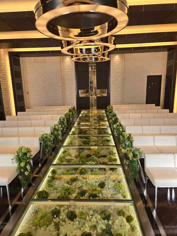 ガラス張りのバージンロードの下に敷き詰められた白と緑の花々が、清楚で素敵な雰囲気を演出していました。