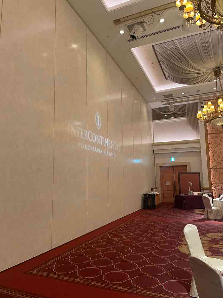 モナコニース会場後方にもロゴが映し出されていた、ボルドーの絨毯とシャンデリアが重厚感を出していた