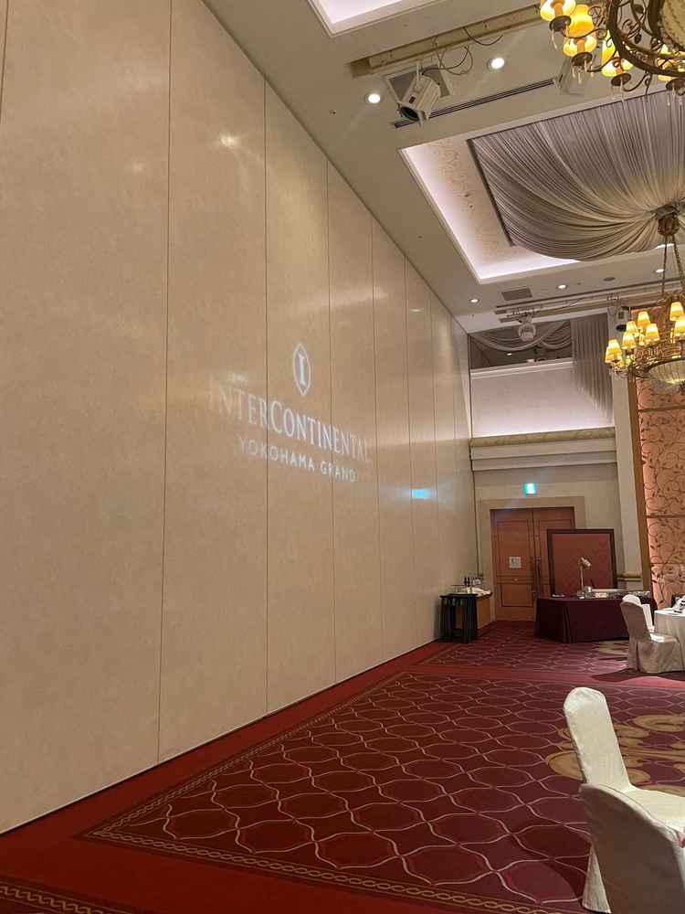 モナコニース会場後方にもロゴが映し出されていた、ボルドーの絨毯とシャンデリアが重厚感を出していた