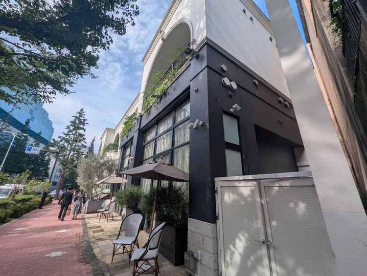 ​白と黒を基調としたモダンでおしゃれな外観。街路樹の緑やパラソル付きのオープンテラスが心地よいです。