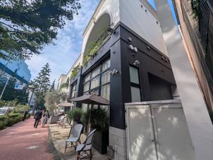 ​白と黒を基調としたモダンでおしゃれな外観。街路樹の緑やパラソル付きのオープンテラスが心地よいです。