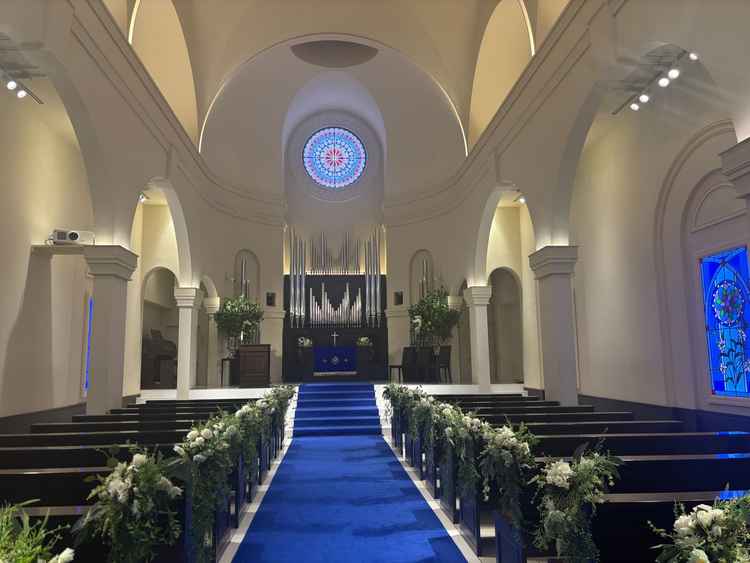 挙式場は聖堂で青の絨毯はドレスが映えるようにされている。ステンドグラスは自然光ではないため暗くできる