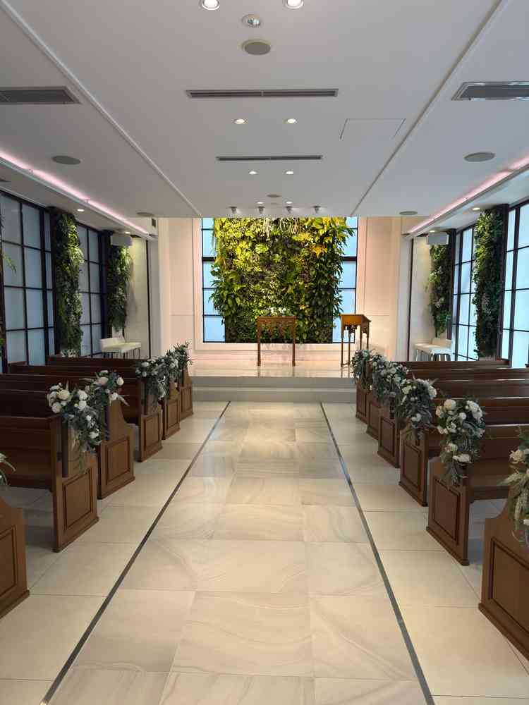 キリスト教式の挙式場で木目調の座るイス、後ろが植物のグリーン基調であり自然を感じられます。