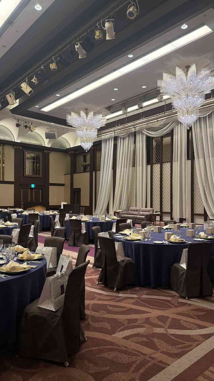 披露宴会場。天井が高く、シャンデリアや新郎新婦が座る席の後ろのカーテンが豪華に感じた。