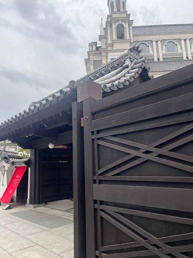 百花籠の入口の写真。日本邸宅の和風の雰囲気を醸し出す門から中世ヨーロッパの建物のような教会が見える。