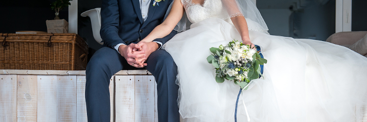 ウェディングドレスの新婦と並んで座り手を取り合うスーツ姿の新郎