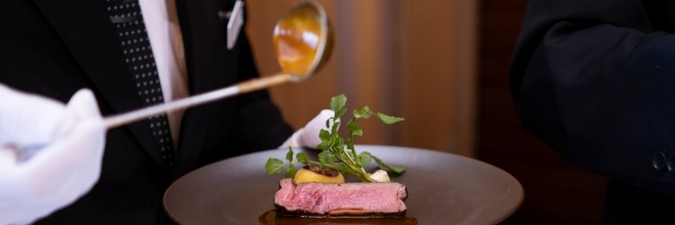 肉料理にソースをかけるスタッフの手元