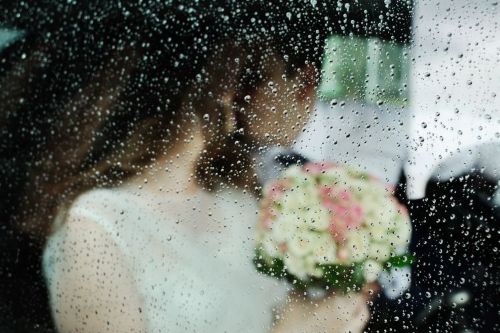 雨粒がついた窓越しに見えるブーケを手にした新婦